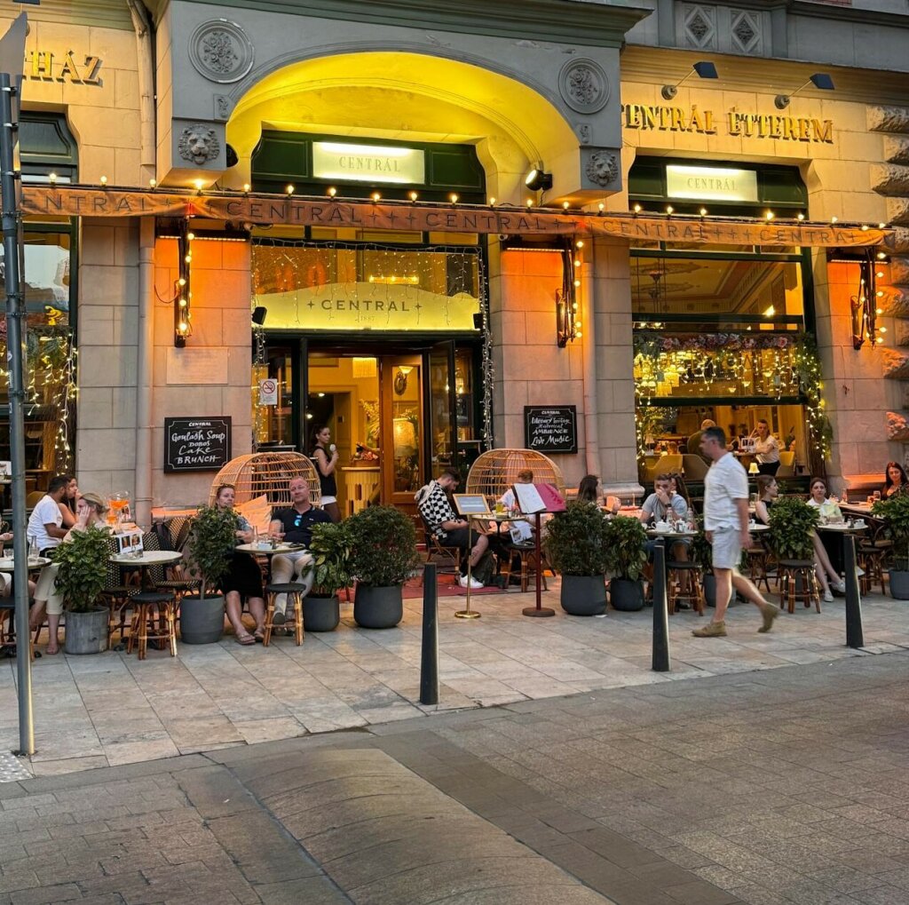 Ζεστή βραδινή ατμόσφαιρα έξω από café στη Βουδαπέστη με ταξιδιώτες και ντόπιους.